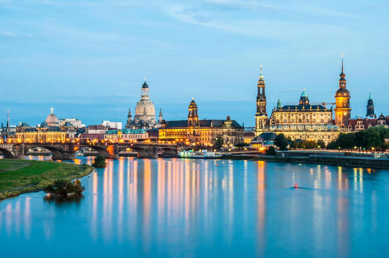 Das Bild zeigt die berühmte Dresdner Frauenkirche und die umliegende Altstadt am Abend, gespiegelt in der Elbe