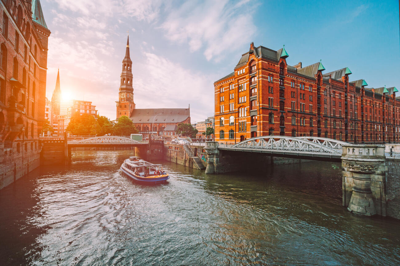 Touristic cruise boat on a channel with bridges in the old warehouse district Speicherstadt in Hamburg in golden hour sunset light, Germany.